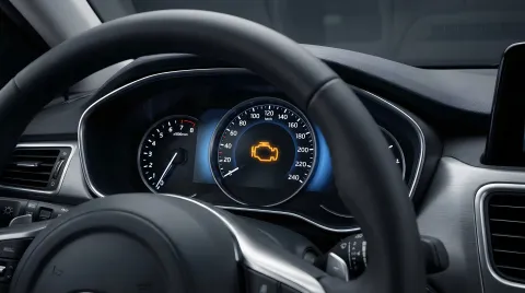 Vehicle dashboard displaying an illuminated check engine warning light viewed from the driver's seat.