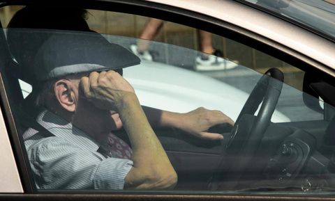 Driver sitting in a hot car appearing frustrated while dealing with weak air conditioning during summer heat.