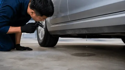 ASE-certified mechanic inspecting water leaking under a car after the air conditioner has been running.