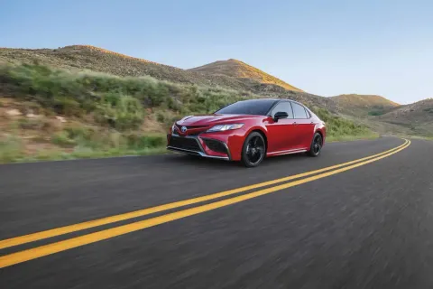 Red Toyota Camry Hybrid driving on an Arizona desert highway, illustrating hybrid battery replacement and ownership for Arizona drivers.