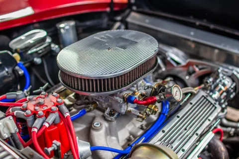 Close-up of a carburetor on a classic car engine, showing the air cleaner removed and fuel delivery components.